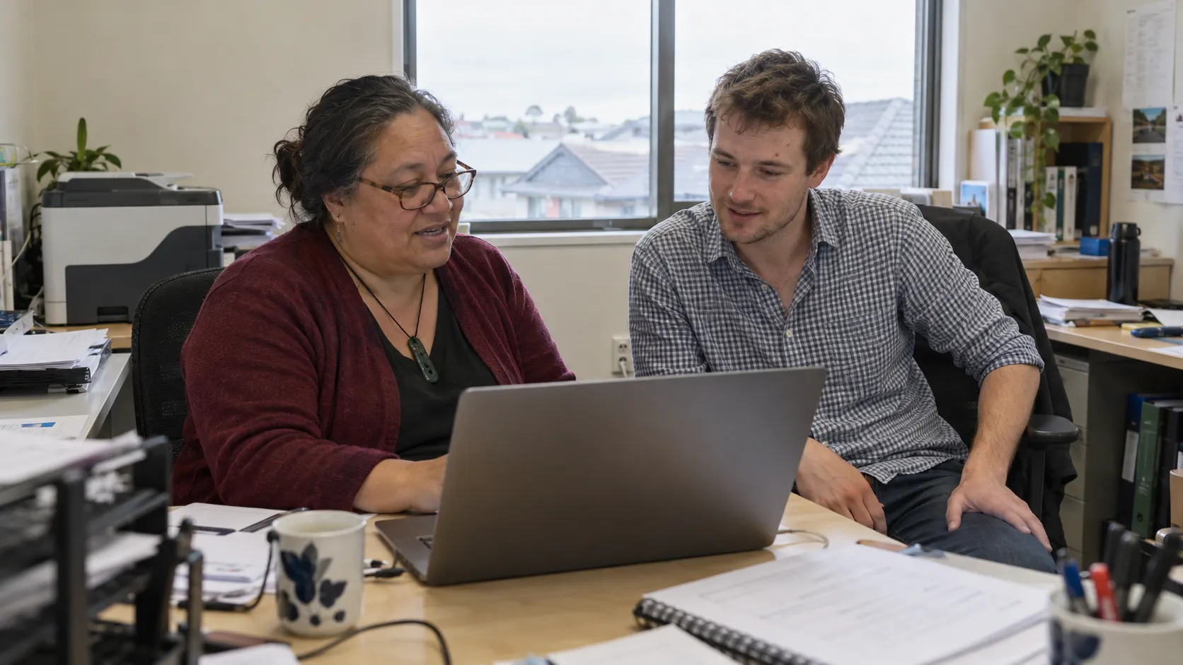 Illustrative scene of two colleagues discussing work at a laptop in a small suburban office